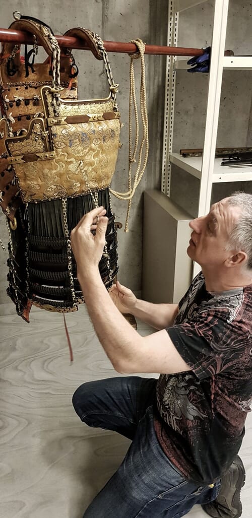 David Thatcher relacing the dō of a Japanese armour on a makeshift frame during on site restoration