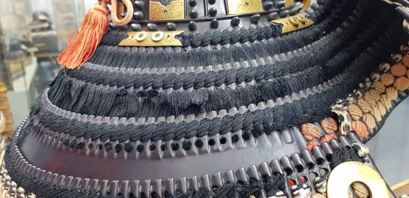 Close up of a Japanese kabuto shikoro showing rotted black odoshi lacing prior to restoration